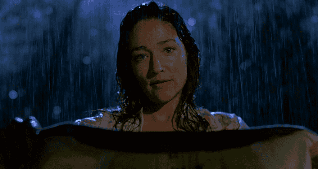A woman stands in the rain, holding out a blanket or cloth. She appears soaked, with water dripping from her hair. The scene bears an eerie familiarity to the opening moments of a suspenseful tale, as if hinting at the beginning of a chilling chapter in the Psycho franchise.