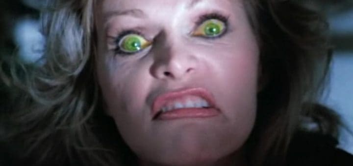 A woman with wide, green glowing eyes and a contorted, angry expression stares intensely at the camera, her teeth clenched and lips curled back—certainly not the usual "Happy Birthday To Me" mood.