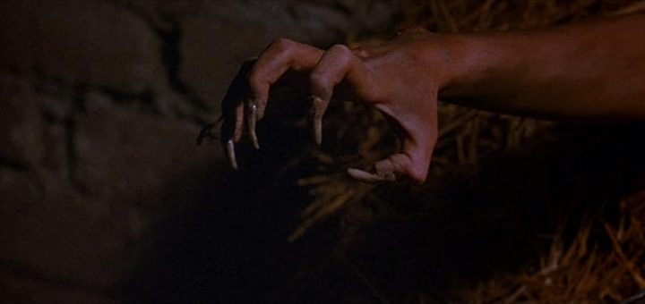 A close-up of a hand transforming into a clawed, monstrous shape with long, pointed fingernails, set against a dimly lit, rough background with a hint of straw.