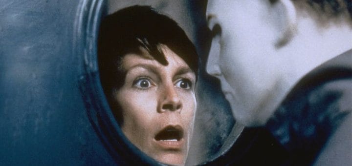A terrified woman with short dark hair stares through a circular window at a blank-faced figure in a white mask, evoking the tense and suspenseful atmosphere of a classic cult film or vintage horror movie.