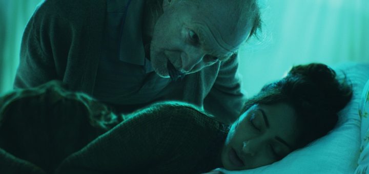 An older man with a concerned expression leans over a young woman sleeping peacefully in bed. The room is dimly lit with a greenish hue, creating a serene yet mysterious atmosphere, as if waiting for further instructions to unfold.