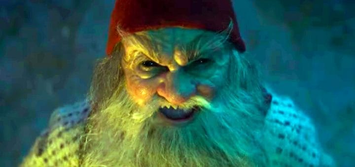 A close-up reveals a fictional character with a white beard, wearing a red hat and patterned shirt. With a fierce expression, he's eerily illuminated by blue and green lights as if hinting there's something in the barn waiting to be discovered.