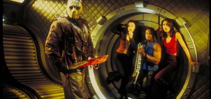 A masked figure holds a bloody machete in a futuristic room. Three people, including two women and a man, appear frightened in the background, standing in a circular doorway with quilted metallic walls and LED lights.
