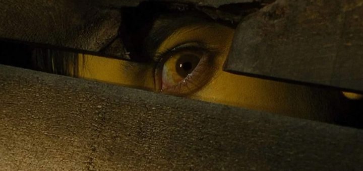 A close-up of a person's eye peeking through a narrow, jagged hole in a wooden surface, with dim lighting creating suspense and mystery, reminiscent of the chilling scenes in the 2006 horror movie Black Christmas.