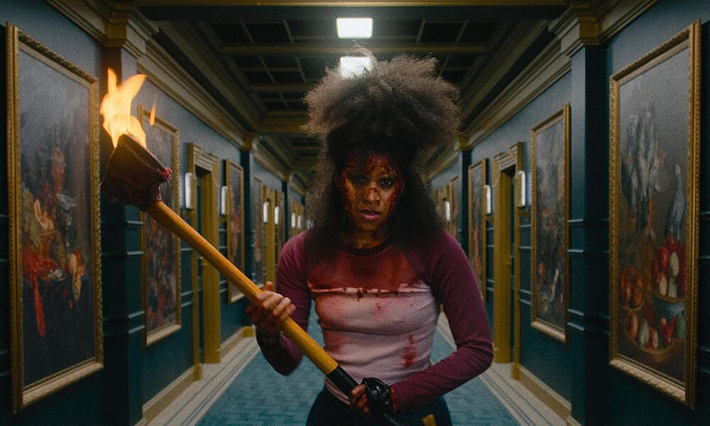 A woman with wild hair and a blood-stained shirt holds a flaming torch, standing in a hallway lined with framed paintings. The intense and dramatic scene evokes the chilling atmosphere of A Nightmare On Elm Street 4: The Dream Master.